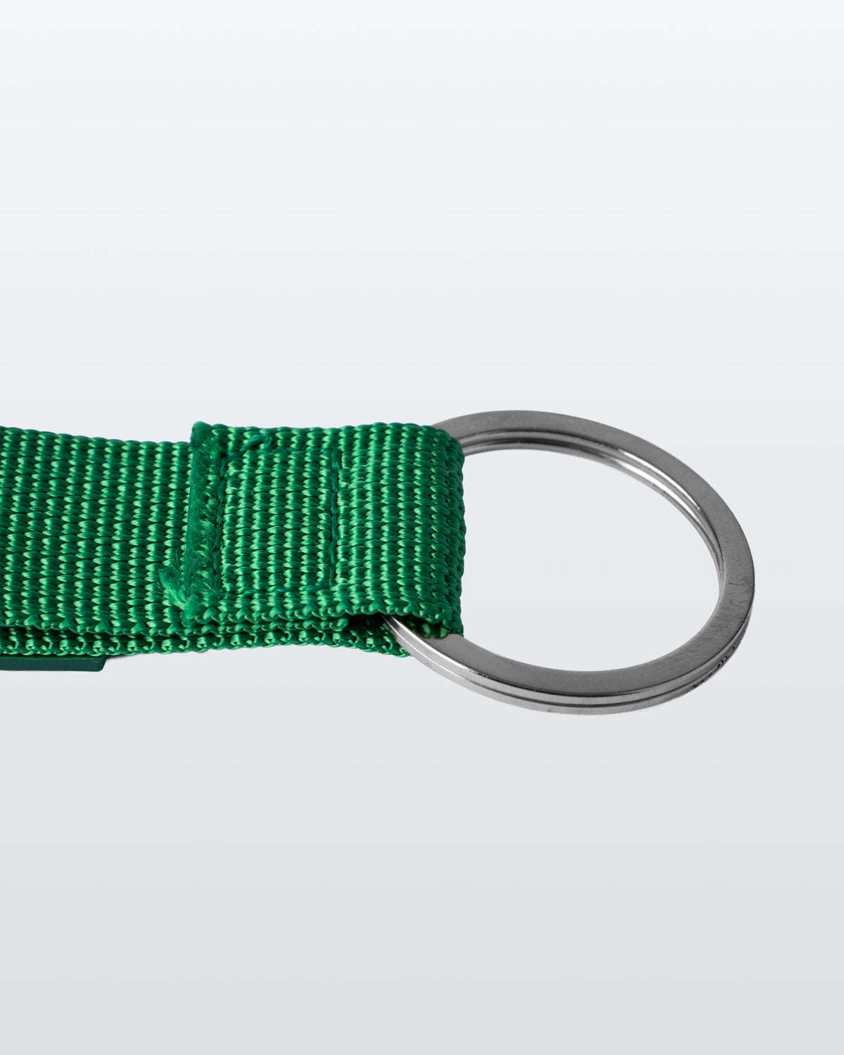A close-up of a bright green woven webbing strap attached to a silver metal O-ring, shown against a light gray background.