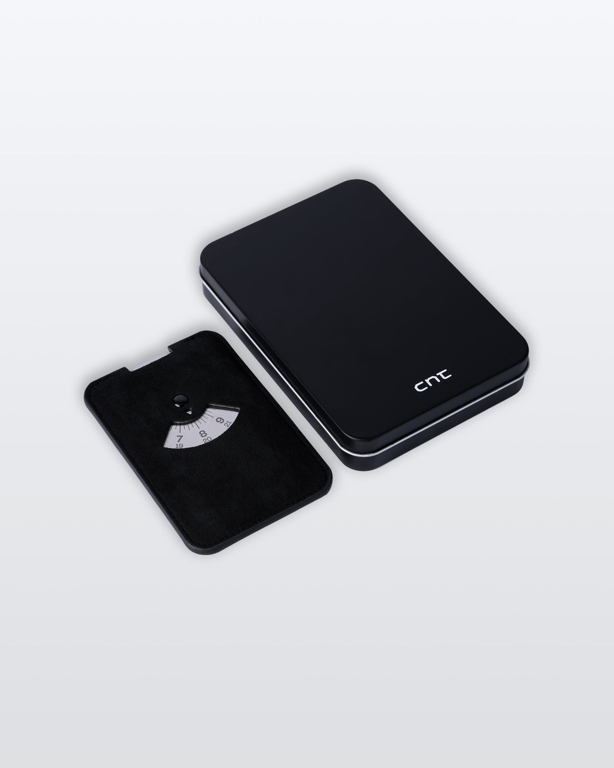 A black alcantara parking disc with silver disc, with its metal box with a white cnt logo beside it on a clean light gray background. 